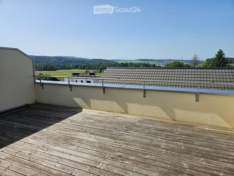 Wooden deck with metal railing, overlooking a rural landscape with fields and trees.