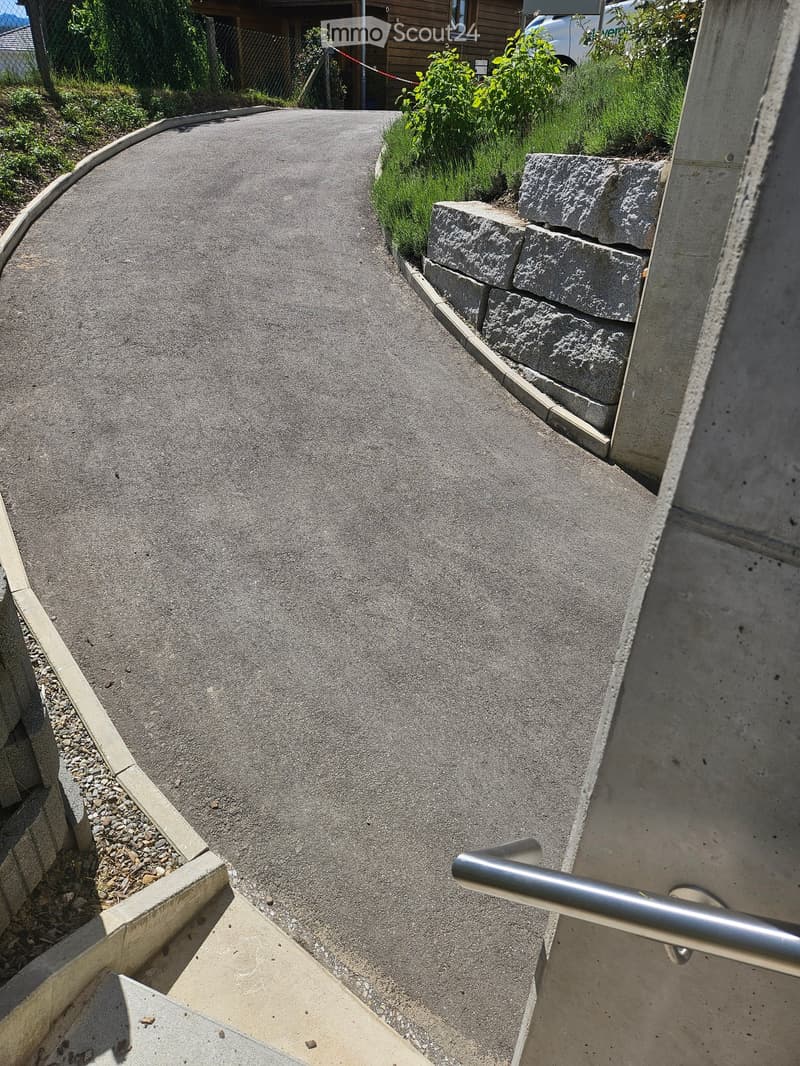 A concrete pathway bordered by stone steps and greenery, with a metal handrail on one side.