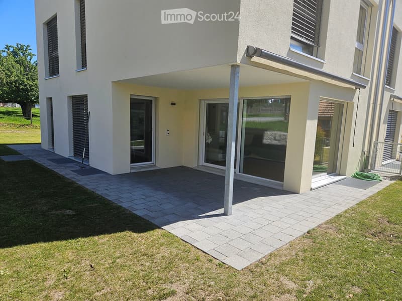 Modern house exterior with a covered patio area, large sliding glass doors, and a well-maintained lawn.