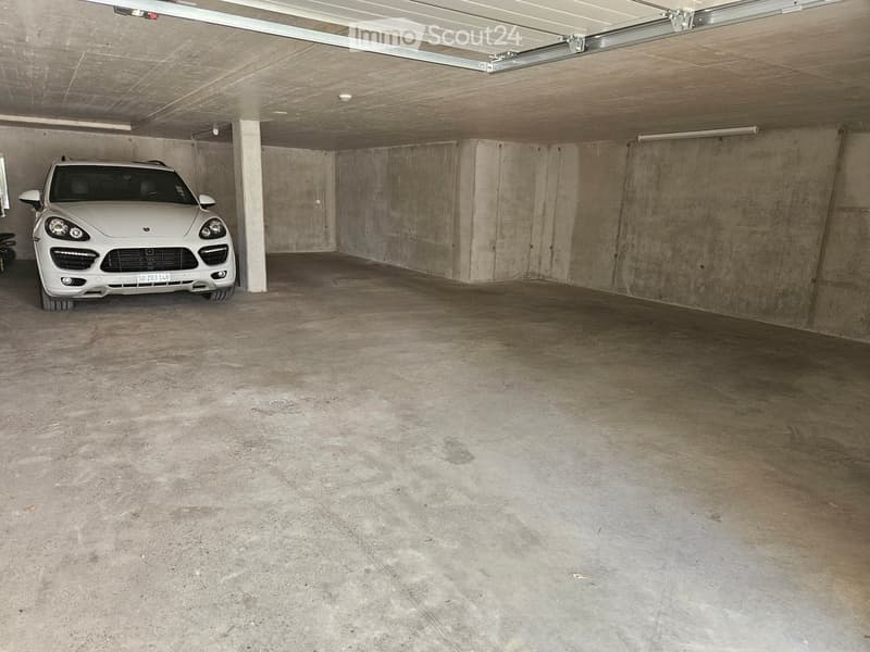 Underground garage with concrete walls and floor, one parked car, and exposed ceiling beams.