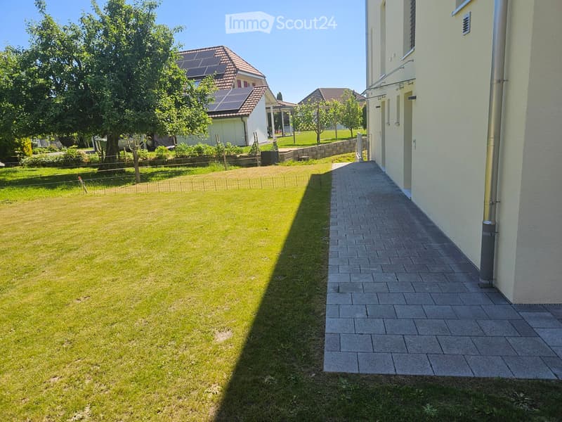 Well-maintained garden with a neatly trimmed lawn, a paved pathway leading to a house, and surrounding greenery including trees and shrubs.