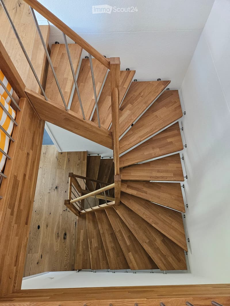 Spiral staircase with wooden steps and metal balustrade, leading to an upper level.