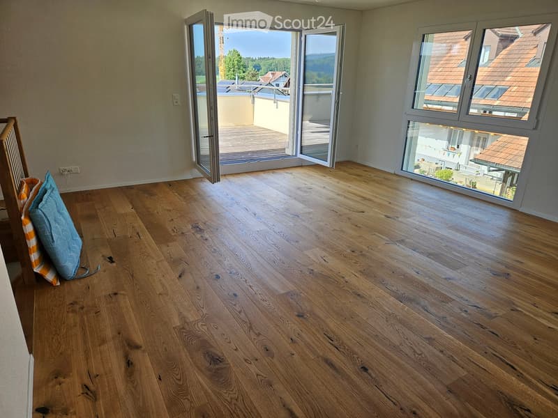 Empty room with wooden flooring, large windows, and sliding doors leading to a balcony.