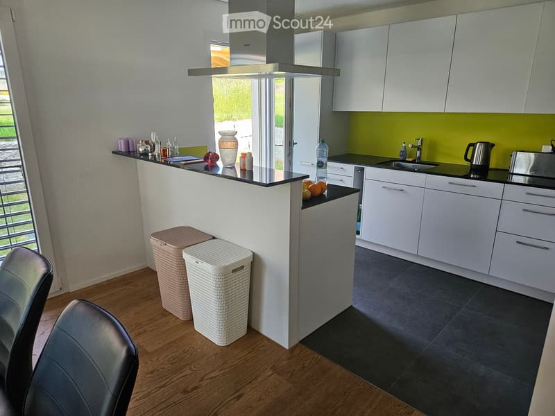 Modern kitchen with white cabinets, black countertops, and a central island. Features include a sink, faucet, and various kitchen items on the counter.