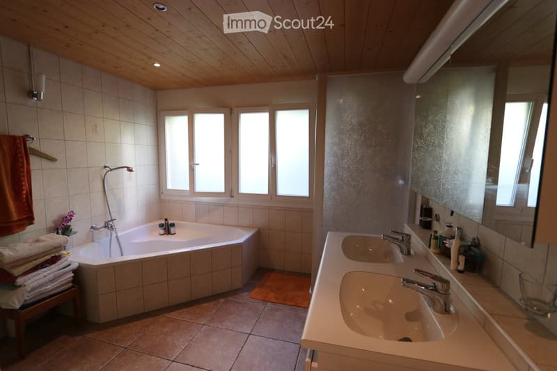 Bathroom. Bathroom with a bathtub, double sink, mirror, and tiled walls. Features a wooden ceiling, multiple windows, and a towel rack with folded towels.