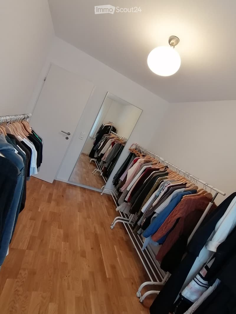 A room with a large mirror, a rack of clothes, and a wooden floor.