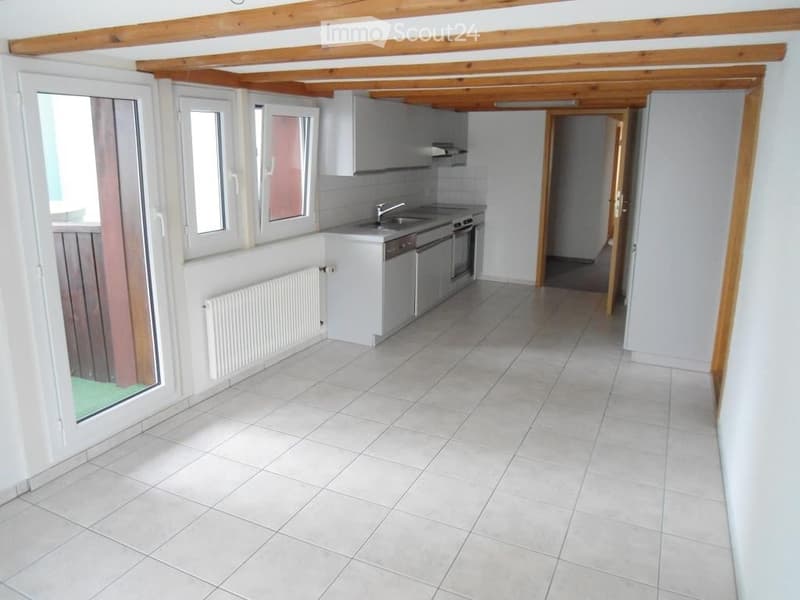 Bright, modern kitchen with white tiled flooring, white cabinets, and stainless steel appliances including a sink, faucet, oven, and dishwasher. A radiator is visible on the wall, and the space has large windows allowing natural light.