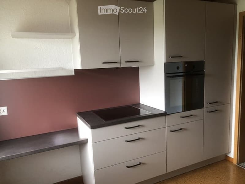 Modern kitchen with white cabinets, a black countertop, and built-in oven. Features sleek design with metallic handles and a dark backsplash.