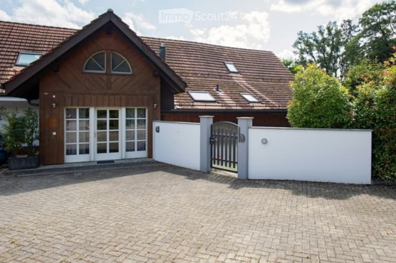 Two-story house with a wooden facade, red-tiled roof, large garage, and a gated driveway.