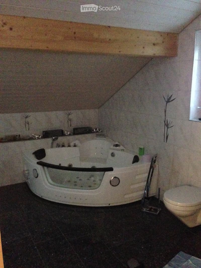 Bathroom with a large bathtub, toilet, and a mirror above the sink. The walls are painted in a light color, and the floor is tiled.