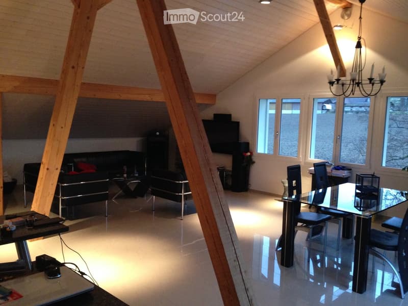 Open-plan living and dining area with exposed wooden beams, modern furniture, and large windows.