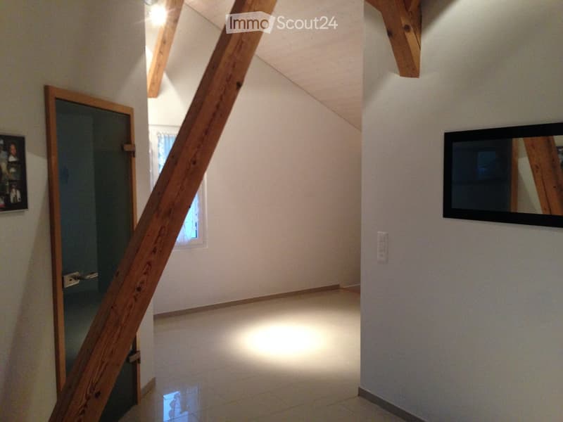 Empty hallway with wooden beams, tiled floor, and a mirror on the wall. A door leads to another room with a window visible.