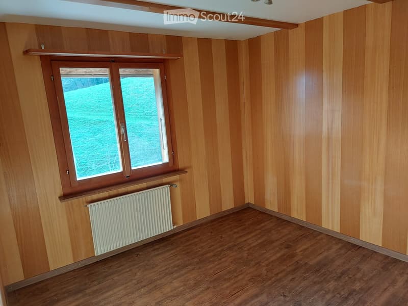 Empty room with wooden walls, wooden floor, and a window with a radiator below it.