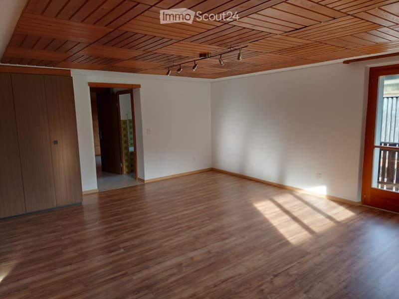 Empty room with wooden flooring, white walls, and a wooden ceiling with track lighting. Features a large window with blinds and a door leading to another room.