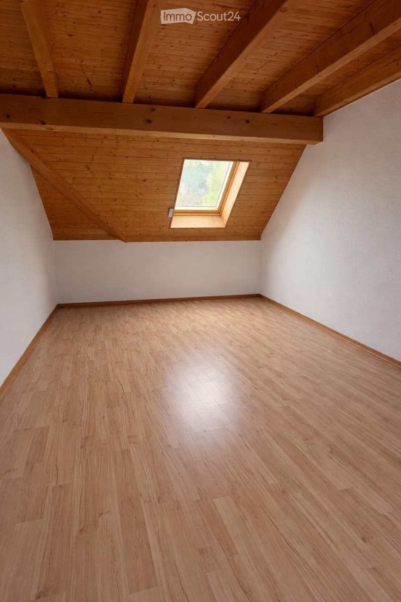 Empty room with wooden flooring and exposed wooden ceiling beams, featuring a skylight window in the sloped ceiling.