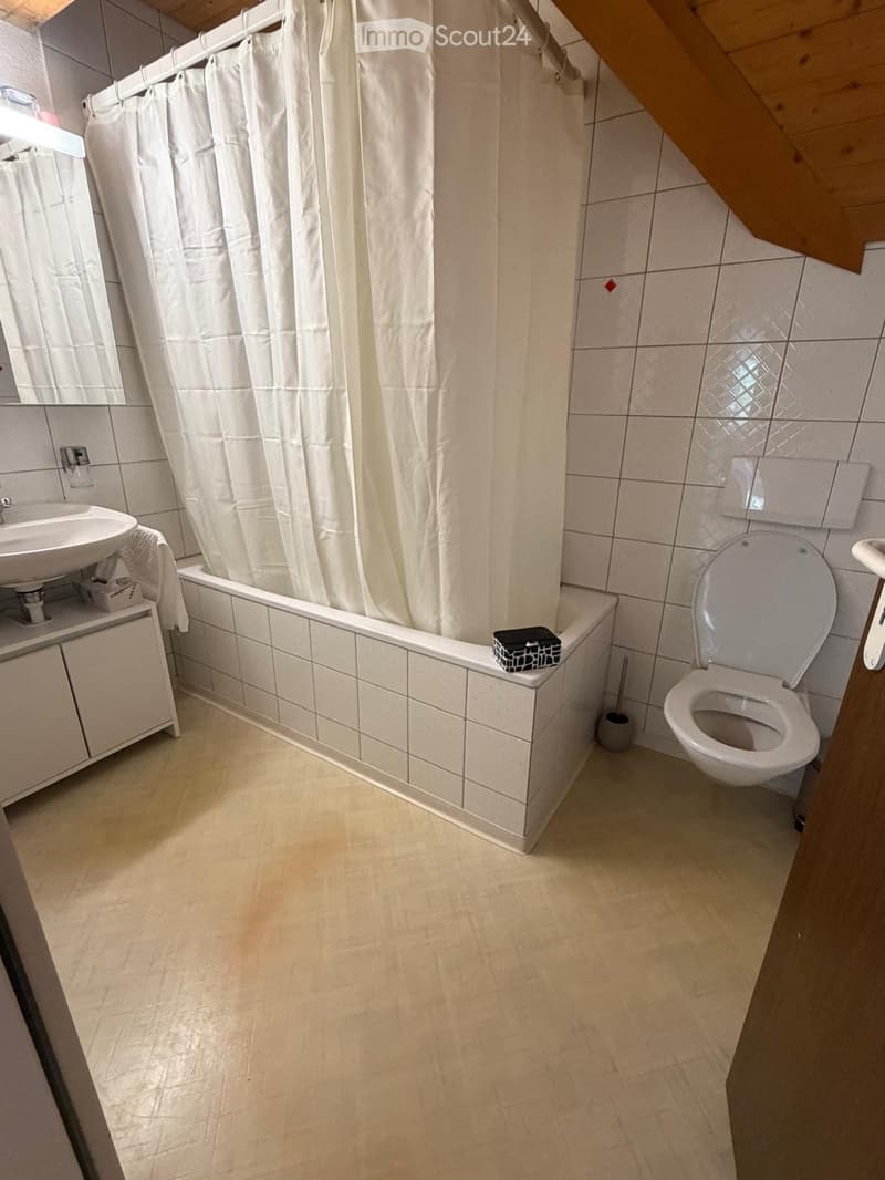 Bathroom with a white tiled bathtub, a toilet, a sink with a cabinet, and a mirror above the sink. The room has beige tiled walls and a light-colored floor.