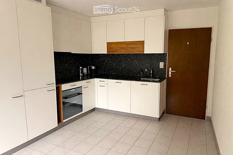 Modern kitchen with white cabinets, black granite countertop, and tiled floor. Features a sink, faucet, oven, and coffee maker on the counter.