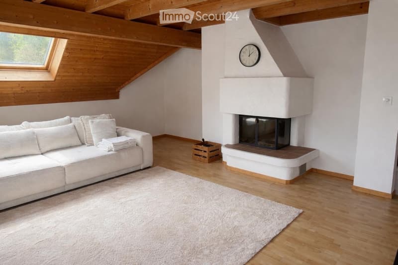 Bright living room with wooden beams, white walls, a white sofa, a fireplace, and a large window letting in natural light.