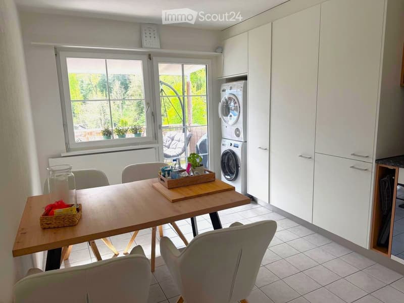 Bright room with a wooden dining table, chairs, a washing machine, and white cabinets.