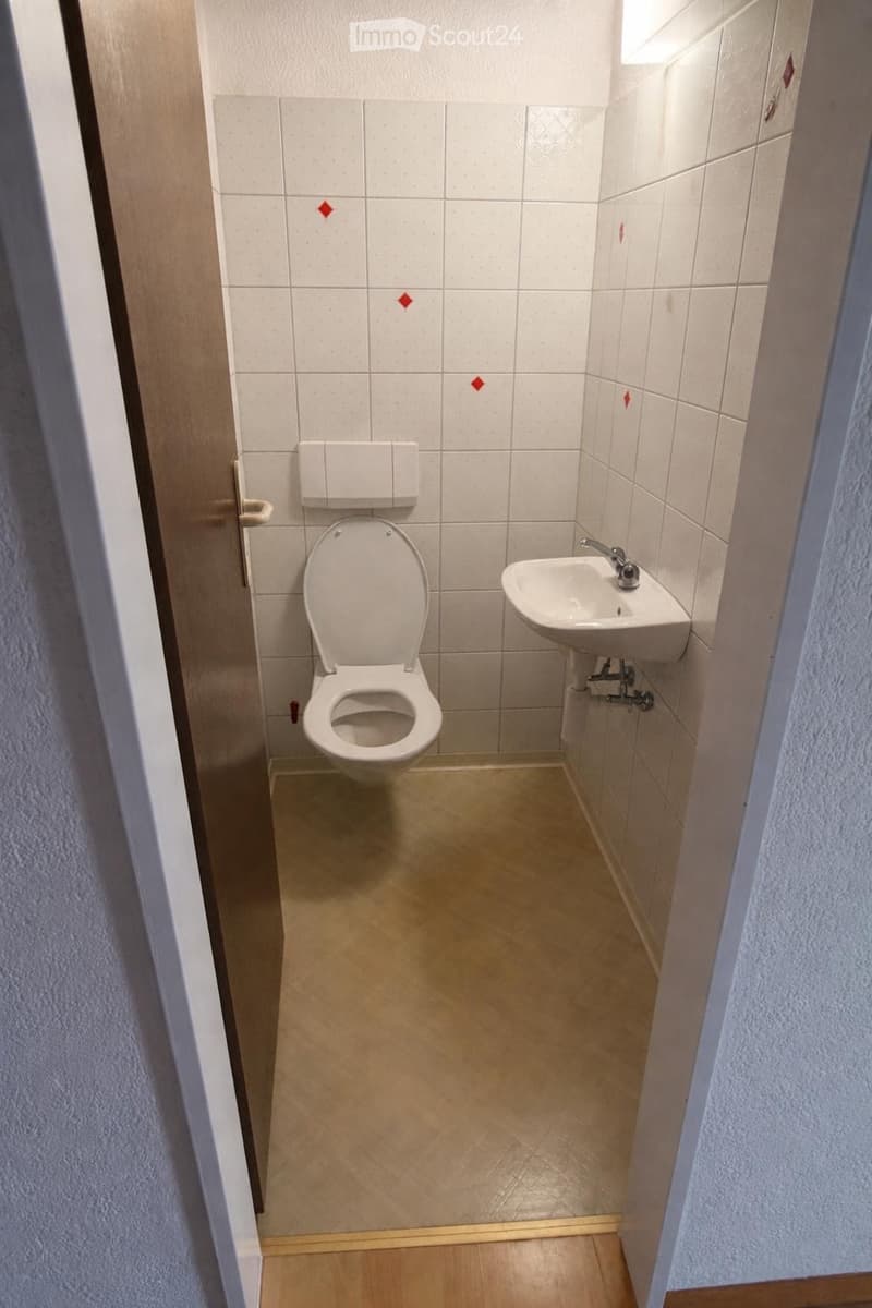 Small bathroom with white tiled walls, a toilet, and a sink. The floor is light-colored wood.