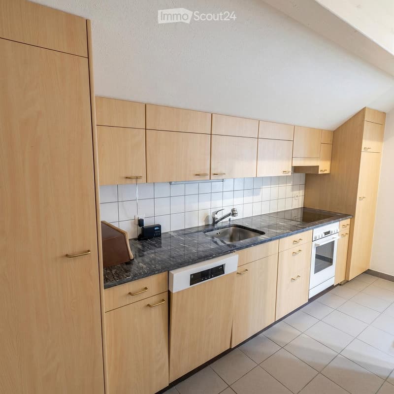 Modern kitchen with light wooden cabinets, granite countertop, stainless steel sink and faucet, built-in dishwasher, and oven.