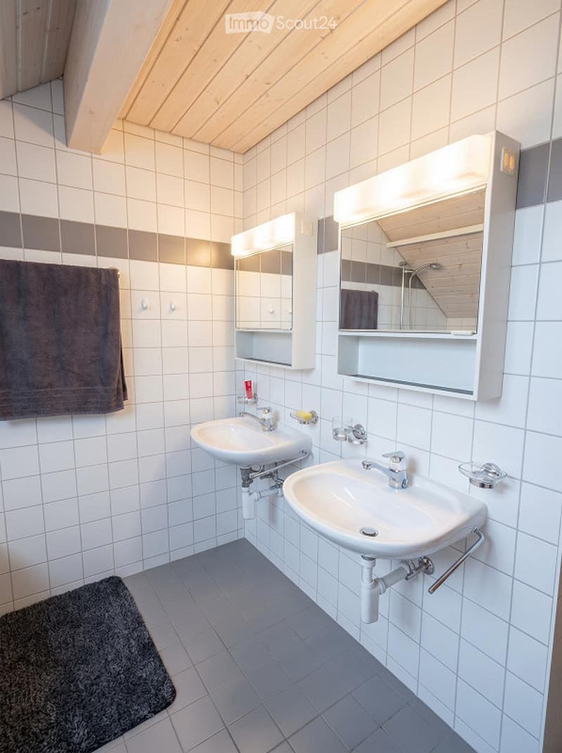 Modern bathroom with two sinks, built-in mirrored cabinets, white tiled walls, and a dark towel on the left side.