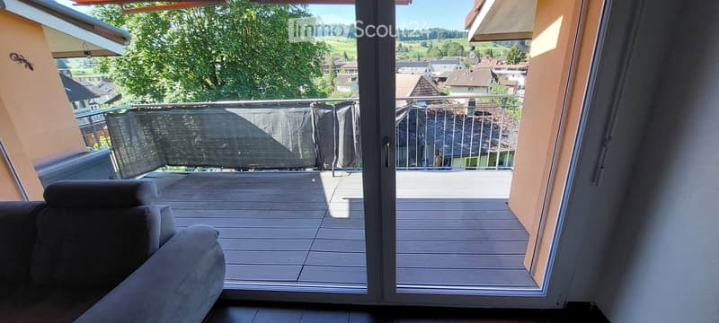 Balcony with wooden decking, metal railing, and a view of a green landscape and houses.