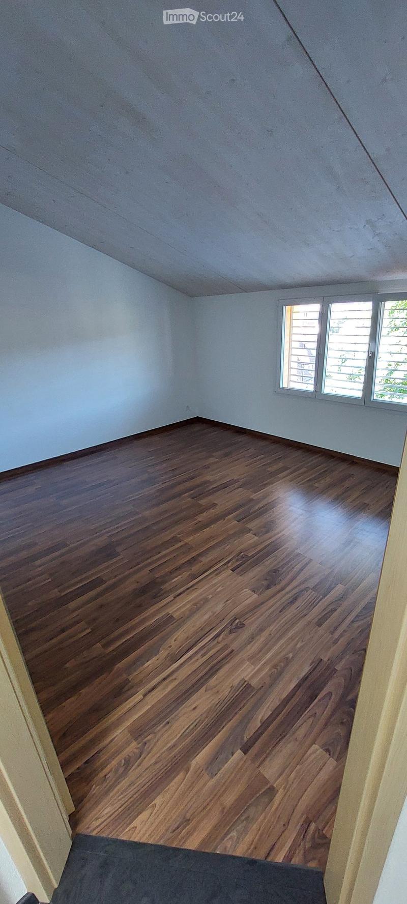 Empty room with wooden flooring and white walls, featuring a window with blinds on the right side.