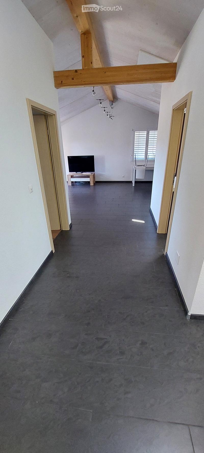 An attic space with exposed wooden beams, grey tiled floor, and a small TV setup on a stand near the entrance.