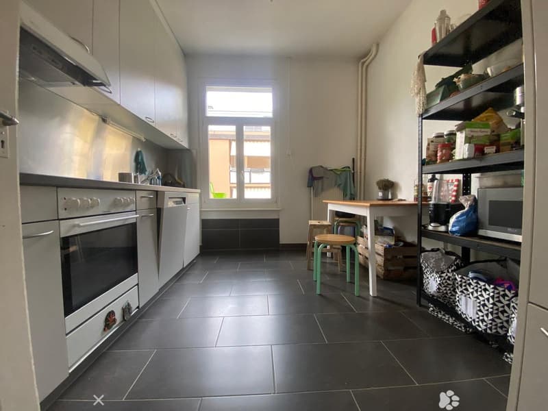 Modern kitchen with stainless steel appliances, black tiled floor, and a wooden table with stools.