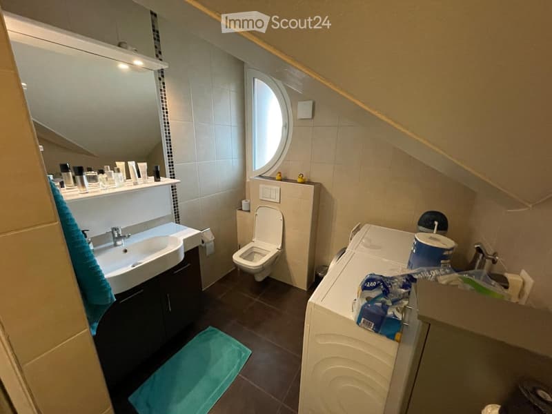 Modern bathroom with a sink, toilet, bathtub, and mirror. Includes toiletries on the sink counter and a towel on the floor.