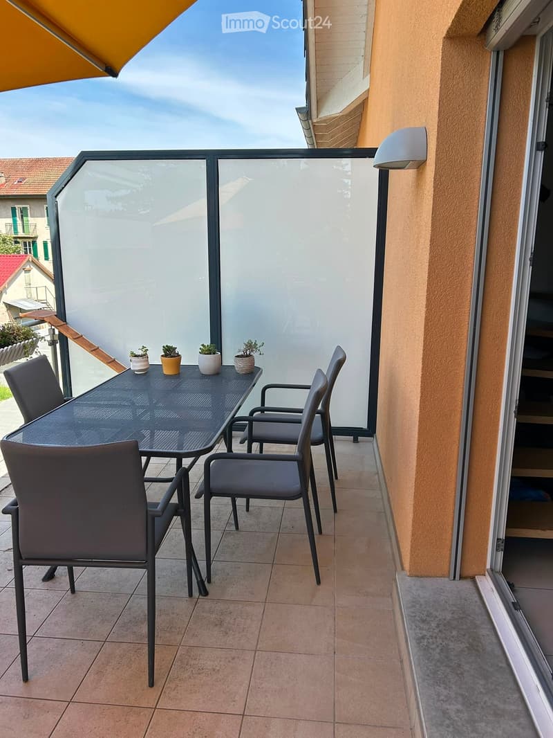 Balcony with tiled floor, black metal table, four chairs, and four small potted plants.