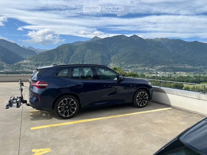 A dark blue SUV with a caravan attached is parked on a raised ground floor with a scenic mountain view in the background.