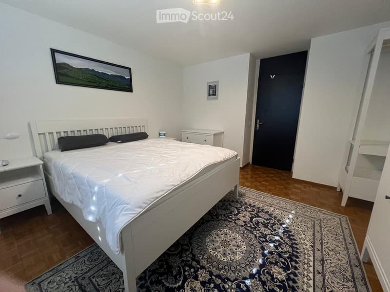 Bedroom with a white bed, nightstands, and a patterned rug on a wooden floor.