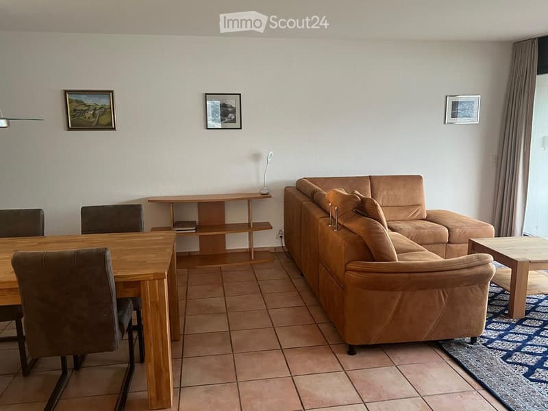 Living room with a large sectional sofa, wooden dining table, chairs, a shelf, and picture frames on the wall.