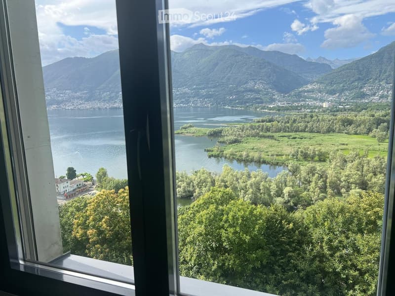 View from a balcony showing a lake, mountains, and a town in the distance.
