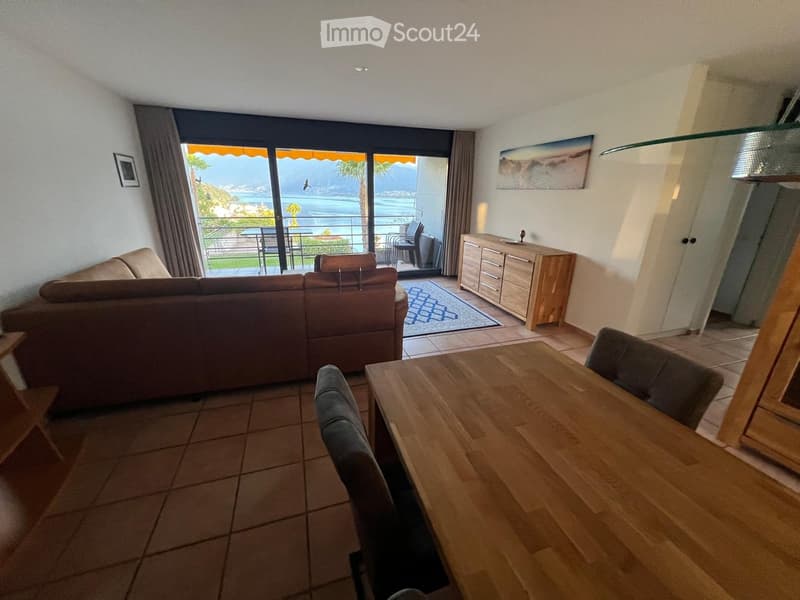 Bright living room with a view of the sea, featuring a sofa, dining table, chairs, and a cabinet.
