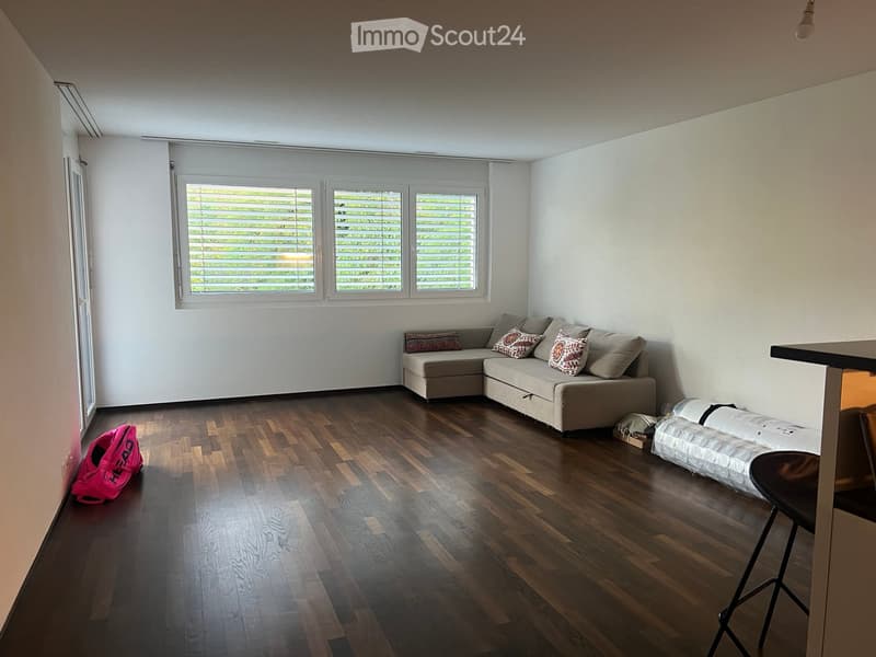 Living room with wooden flooring, large windows, a beige sectional sofa, and a pink handbag on the floor.