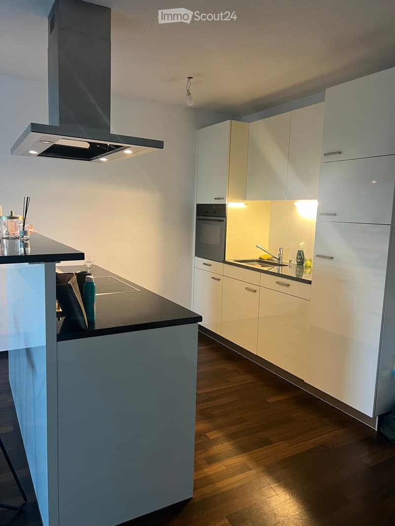 Modern kitchen with white cabinets, black countertop, built-in oven, and a small island with a stool.