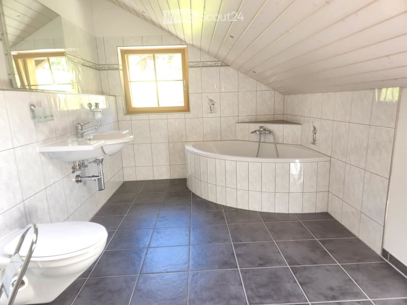 Bathroom with a white sink, bathtub, and toilet, featuring light-colored tiles and a dark tiled floor. A window with wooden frame provides natural light.