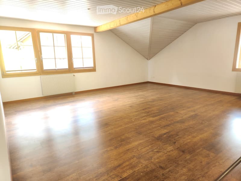 Empty room with wooden flooring, white walls, and large windows with wooden frames. The ceiling has exposed wooden beams and a slanted design typical of an attic space.