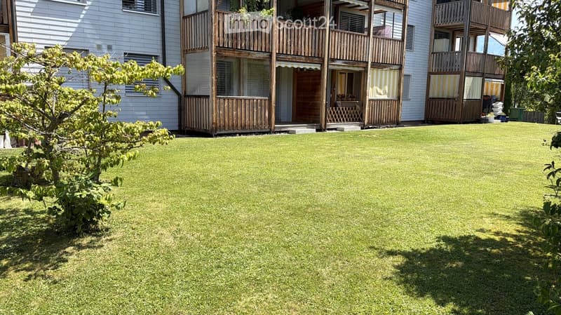 Well-maintained lawn with a small tree, surrounded by a multi-story building with wooden balconies and railings.