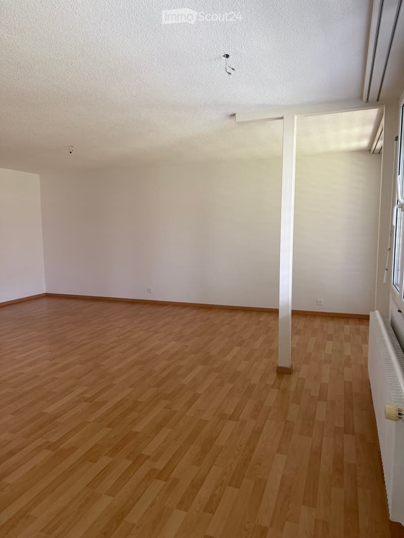 Empty room with wooden flooring and white walls, featuring a radiator and a window with blinds.