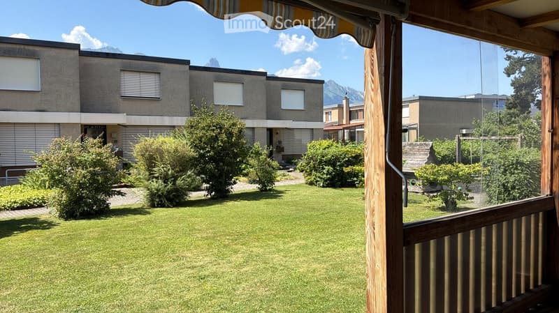 Well-maintained garden with green lawn, trimmed bushes, and a modern building in the background with a scenic mountain view.