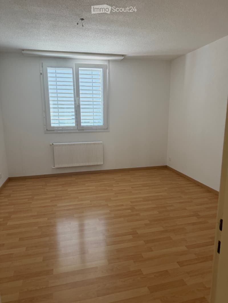 Empty room with wooden flooring, white walls, a window with blinds, and a radiator below the window.