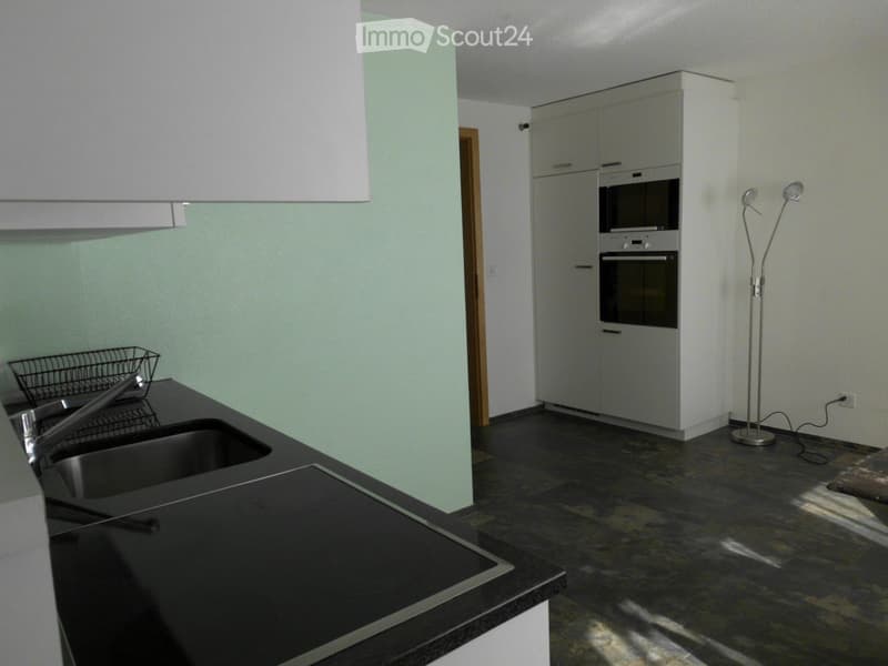 Modern kitchen with dark countertops, stainless steel sink, built-in oven, and white cabinets.