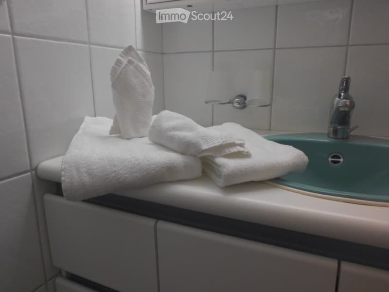 Bathroom with a white tiled wall, a green sink, a chrome faucet, and neatly folded white towels on the counter.