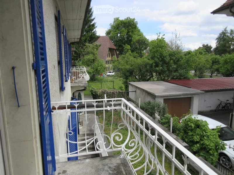 House with balcony, brick and concrete construction, trees, plants, white car