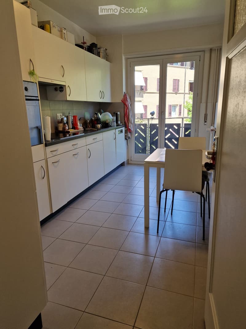 Modern kitchen with white cabinets, stainless steel appliances, tiled floor, and a small dining area with a table and chairs.