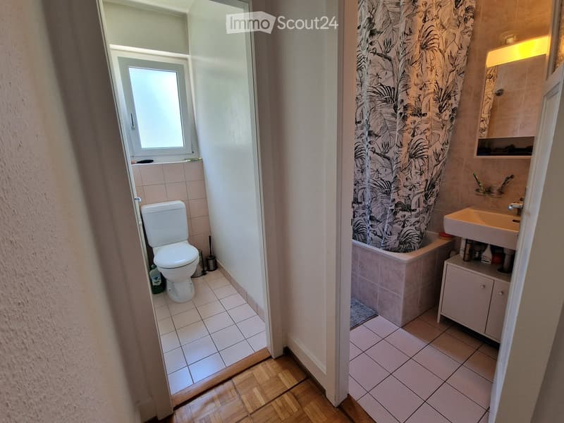 Bathroom with a toilet, bathtub, sink, mirror, and cabinet. The bathtub has a floral shower curtain, and the sink has a mirror above it.